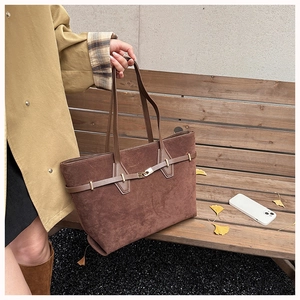 Close-up of brown suede tote bag with golden buckle on a bench with autumn leaves