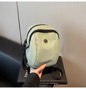 Detail of light green waterproof nylon crossbody bag with circular logo and layered zippers
