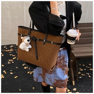 Detail of leopard print tote bag with black leather straps and plush bear charm accent