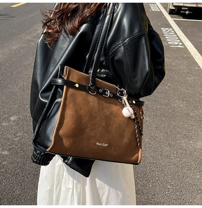 Detailed view of large brown suede patchwork tote bag with baseball pendant and shoulder strap