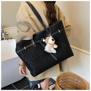 Close-up of black leopard print tote bag with metal buckles and plush puppy charm