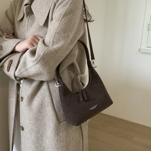 Detail of dark brown suede crescent hobo bag with white logo text on beige wool coat