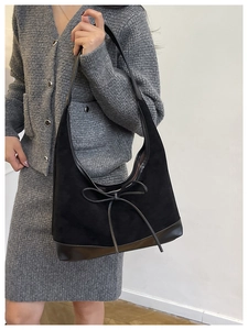 Detail view of black tote bag featuring a decorative large leather bow and suede texture