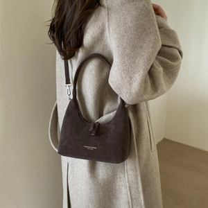 Close-up of brown suede dumpling bag with fashion branding worn by model in coat