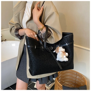 Close-up of black leopard embossed tote bag with plush puppy charm and buckle detail