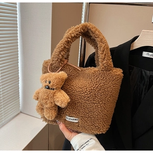 Close-up of brown plush bucket bag with cute bear charm and woven brand label