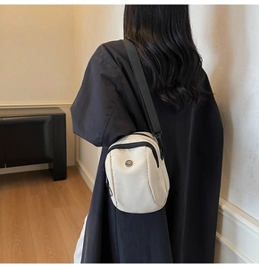 Minimalist cream canvas crossbody bag shown on model with black jacket and adjustable strap