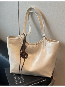 Minimalistische cremeweiße Leder-Einkaufstasche mit Brezel-Anhänger auf Vintage-Büchern