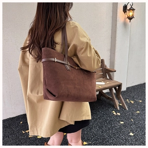 Detail of dark brown suede tote bag with golden buckle and strap on model outdoors