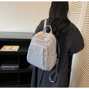 Rear view of a model wearing the light grey multi-pocket faux leather backpack