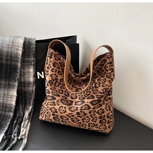 Detail of leopard print canvas tote bag with brown leather handles on dark surface