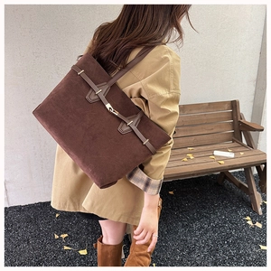 Detail of dark brown suede tote bag with gold buckle on a model in autumn scenery