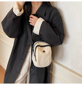 Beige canvas crossbody mini bag with black strap worn by a model in a minimal setting