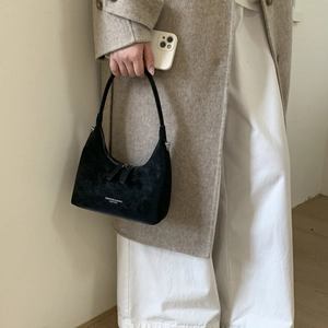Close-up of black matte dumpling bag with white lettering held by model in beige coat