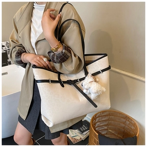 Detail of beige tote bag with black handles and plush puppy charm worn by model