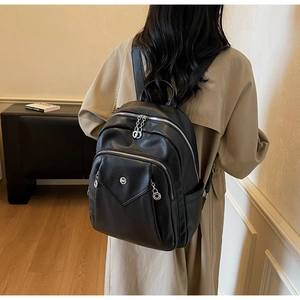 Detailed view of black pebbled leather backpack with silver logo on model in minimalist room