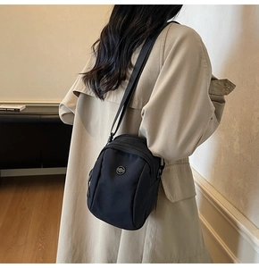 Detail of a black nylon mini crossbody bag with a round metal logo and dual zippers