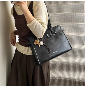 Detail of vintage black leather tote bag with silver buckle and sports-themed charms