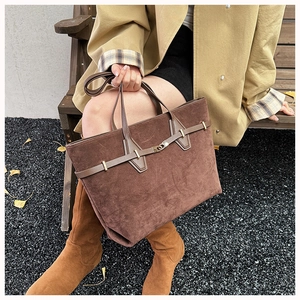 Close-up of a large dark brown suede tote bag with a golden metal buckle for autumn wear