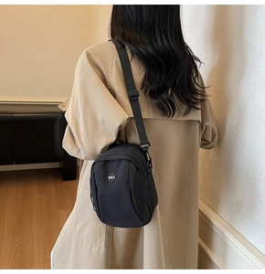 Minimalist black canvas crossbody bag styled with a khaki trench coat in an indoor setting