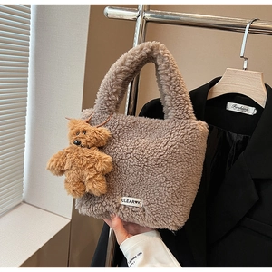 Close-up of brown plush bucket bag with white embroidery and cute bear pendant charm
