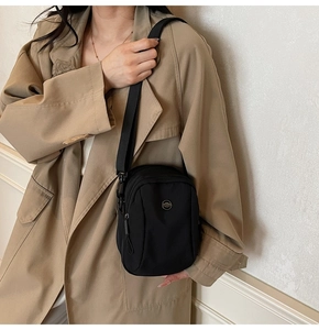 Detail shot of a black canvas crossbody bag styled on a trench coat with adjustable strap