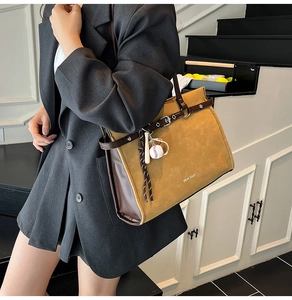 Detail of a large suede tote bag with leather straps and a unique baseball charm