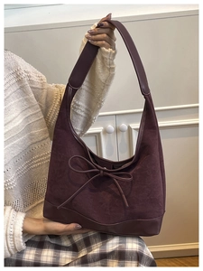 Close-up of deep purple suede tote bag featuring a decorative bow and textured shoulder strap