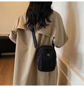 Rear view of a model wearing a small black nylon crossbody phone bag with beige coat