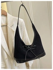 Detail of black suede tote bag featuring a decorative bow on textured cream blazer
