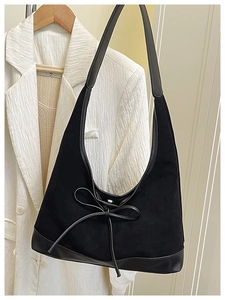 Detail of black suede tote bag with delicate bow knot and smooth leather strap contrast