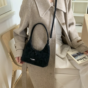 Detail of black suede hobo bag styled with elegant beige coat and white dress