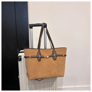 Brown suede tote bag with gold buckle detail mounted on a white suitcase handle