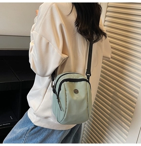 Detail showing the light green canvas crossbody bag worn by a model in a stylish setting