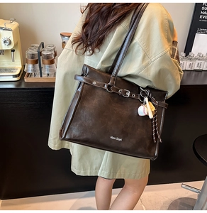 Detail of dark brown leather tote bag with metal buckle and baseball keychain accessory
