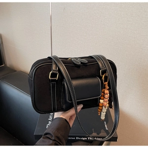 Detail of black suede baguette bag with white stitching and decorative wooden bead tassel