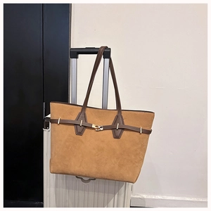 Detail of a large brown suede tote bag with leather straps hanging on a suitcase handle