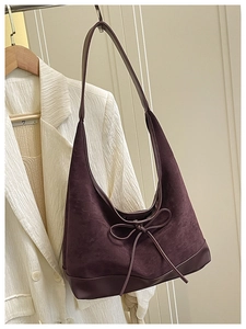 Close-up of deep purple suede tote bag with leather bow detail on white suit background