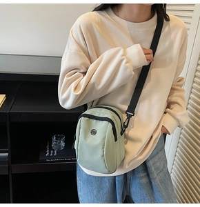 Close-up of mint green nylon crossbody bag with wide black strap and dual zippers
