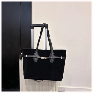 Detail of black tote bag hanging on suitcase handle showing metal buckle and soft texture