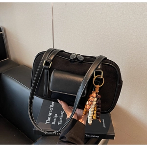 Detail of black suede baguette bag with white contrast stitching and beaded charm