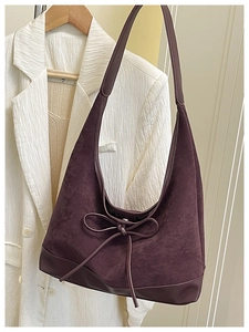Detail view of burgundy faux suede shoulder bag with ribbon bow on white blazer