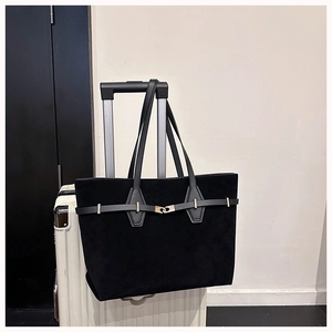 Detail of black suede tote bag with gold buckle on white suitcase for travel