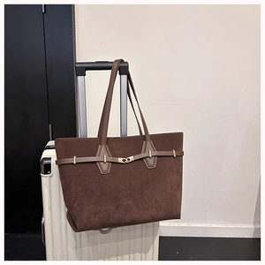 Detail of dark brown suede tote bag with golden buckle mounted on a suitcase