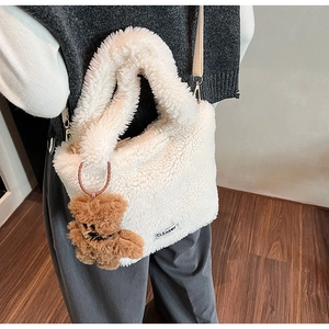 Detail of cream plush bucket bag with teddy bear charm and CLEAR logo patch