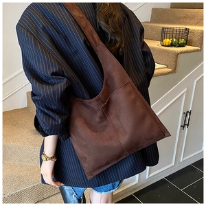 On-shoulder view of a large brown suede bucket bag styled with a striped blazer