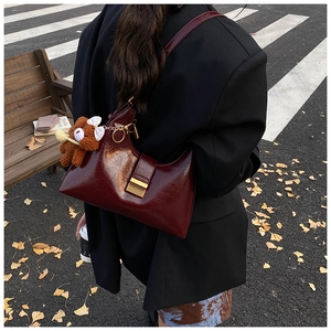 Detail of dark red vintage leather croissant bag with stylish plush bear charm detail