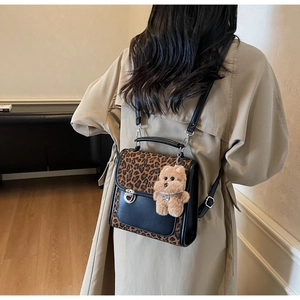 Détail du sac à dos léopard avec charm ours en peluche porté sur un trench beige