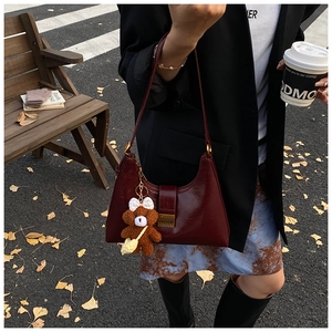 Detail of burgundy patent leather hobo bag with teddy bear charm in autumn street setting