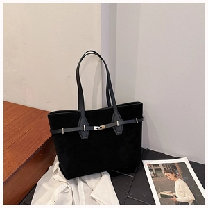 Detail of black suede tote bag with leather strap and metallic buckle in a minimalist setting